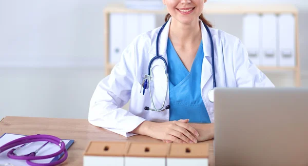 Mooie jonge glimlachende vrouwelijke arts zitten aan het bureau en schrijven. — Stockfoto