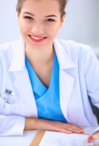 Bonito jovem sorridente médico feminino sentado na mesa . Imagem De Stock