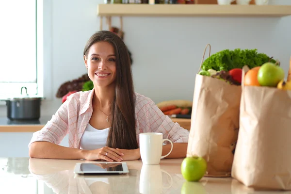 Woman using a tablet computer while drinking tea in her kitchen — Stock Photo, Image