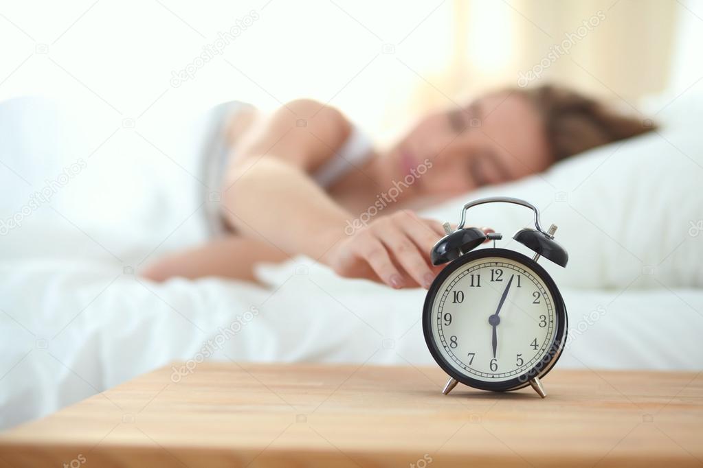 Young sleeping woman and alarm clock in bedroom at home