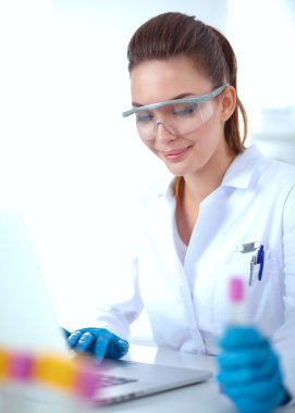 Kadın araştırmacı, beyaz arka planda izole edilmiş ilaç şişeleri ve mataralarla çevrili.