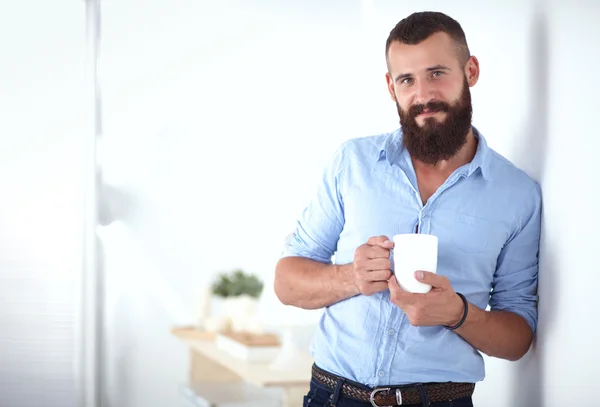 Joven parado cerca de la pared y sosteniendo una taza de café — Foto de Stock