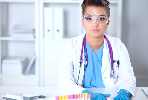 Mooie jonge glimlachende vrouwelijke arts zitten aan het bureau en schrijven. — Stockfoto