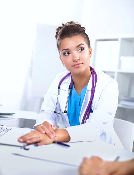 Schöne junge lächelnde Ärztin sitzt am Schreibtisch und schreibt. — Stockfoto