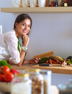 Mutfakta yemek kitabı okuyan genç bir kadın yemek tarifi arıyor.