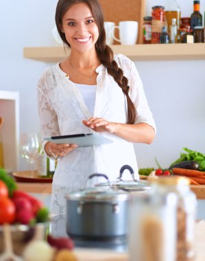Mutfakta yemek yapmak için tablet bilgisayar kullanan genç bir kadın.