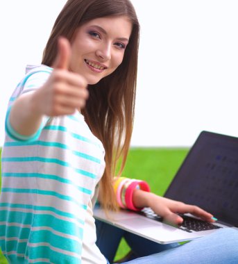 Laptoplu genç bir kadın yeşil çimlerde oturuyor.