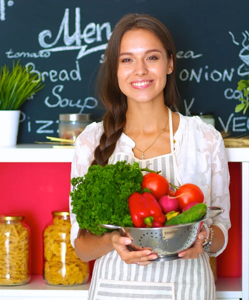 Usmívající se mladá žena drží zeleninu stojící v kuchyni — Stock fotografie
