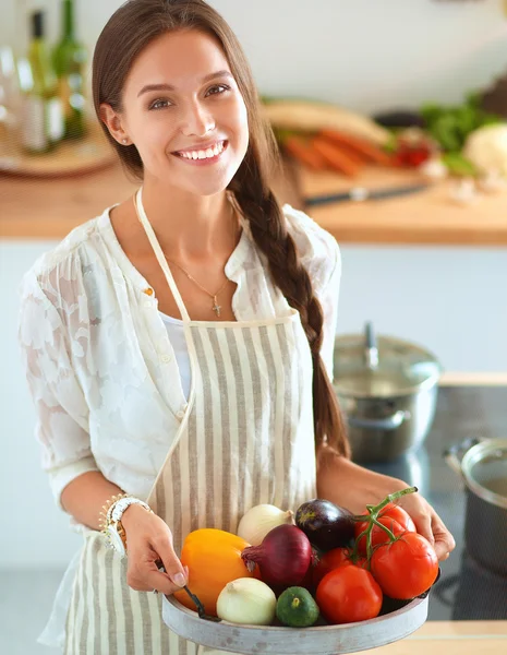 Glimlachende jonge vrouw met groenten in de keuken — Stockfoto