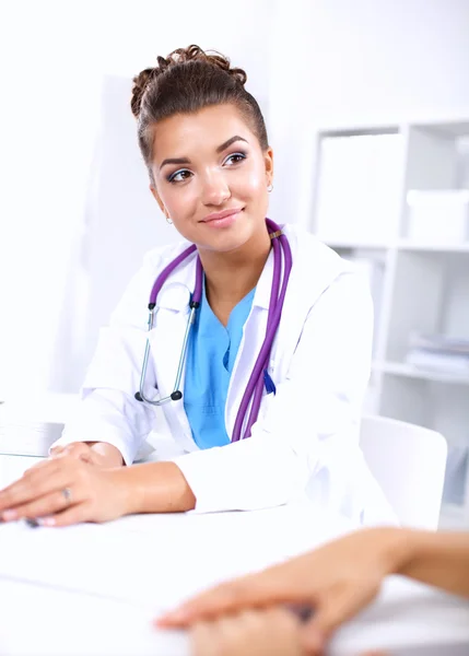 Hermosa joven sonriente doctora sentada en el escritorio y escribiendo. —  Fotos de Stock