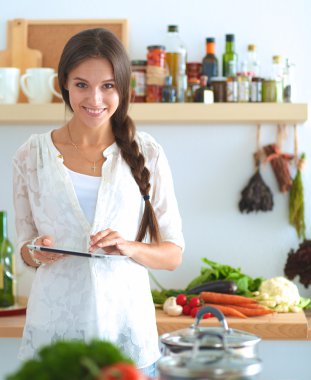 Mutfakta yemek yapmak için tablet bilgisayar kullanan genç bir kadın.