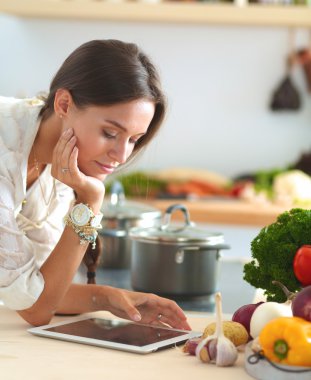 Mutfakta yemek yapmak için tablet bilgisayar kullanan genç bir kadın.