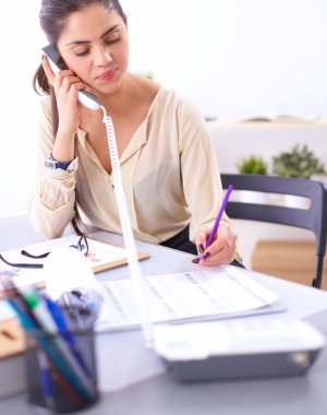 Genç iş kadını masada oturuyor ve telefonla konuşuyor.