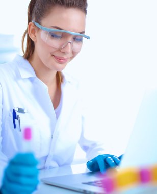 Kadın araştırmacı, beyaz arka planda izole edilmiş ilaç şişeleri ve mataralarla çevrili.