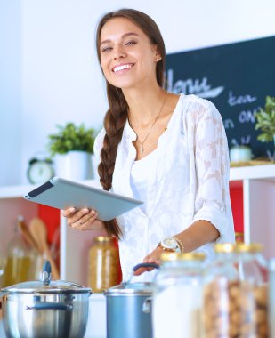Mutfakta yemek yapmak için tablet bilgisayar kullanan genç bir kadın.