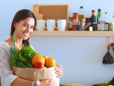 Elinde sebzeli alışveriş torbası tutan genç bir kadın.