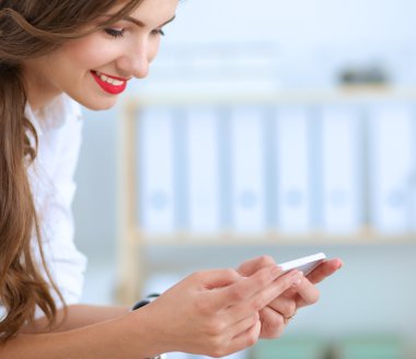 İş kadını ofiste oturan akıllı telefonuyla mesaj gönderiyor.