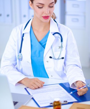 Güzel, genç, gülümseyen bayan doktor masada oturuyor ve yazıyor..