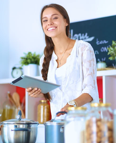 Mutfakta yemek yapmak için tablet bilgisayar kullanan genç bir kadın.
