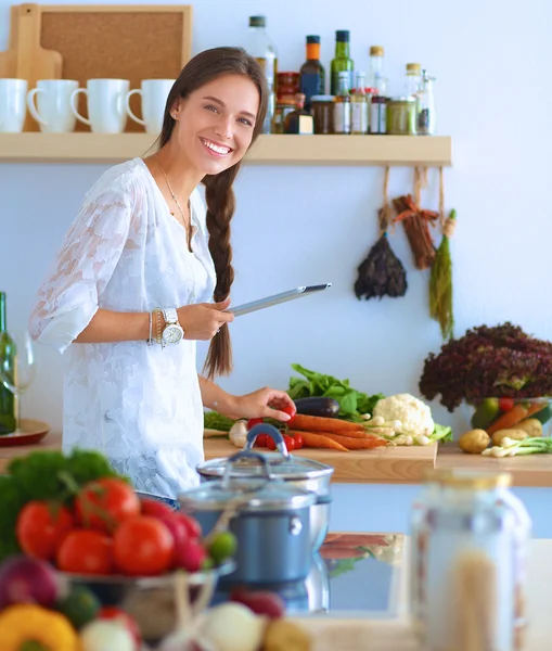 Mutfakta yemek yapmak için tablet bilgisayar kullanan genç bir kadın.