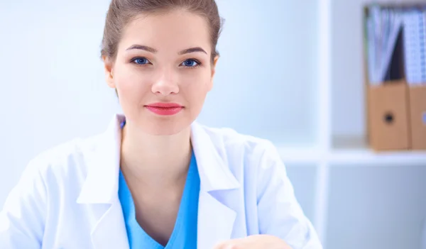 Hermosa joven sonriente doctora sentada en el escritorio . — Foto de Stock