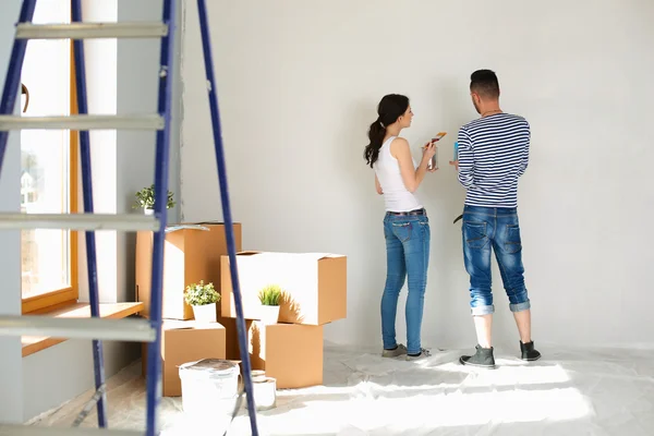 Portret van gelukkig interieur wand via lachende jong koppel-schilderij van nieuwe huis — Stockfoto