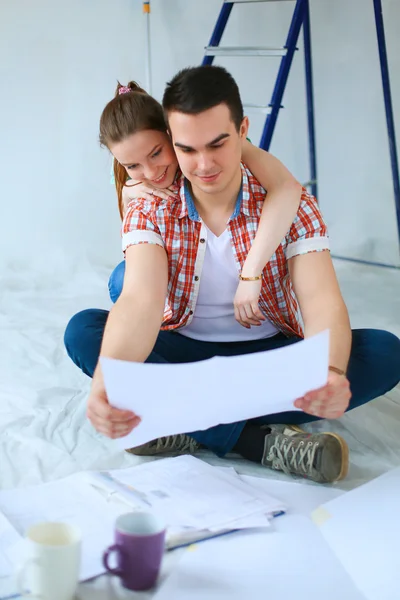 Pareja joven sentada en el piso con plano de apartamento — Foto de Stock