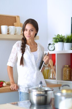 Mutfakta yemek yapmak için tablet bilgisayar kullanan genç bir kadın.