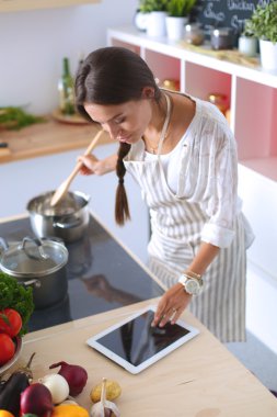 Mutfakta yemek yapmak için tablet bilgisayar kullanan genç bir kadın.