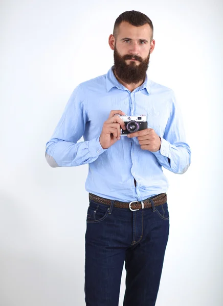 Homem barba jovem segurando uma câmera enquanto de pé contra o fundo branco — Fotografia de Stock