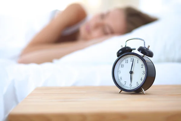 Joven mujer dormida y despertador en el dormitorio en casa —  Fotos de Stock