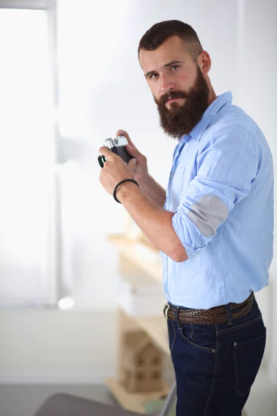 Joven barba hombre sosteniendo una cámara mientras está de pie sobre fondo blanco — Foto de Stock