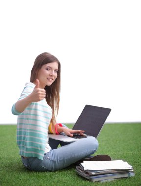 Laptoplu genç bir kadın yeşil çimlerde oturuyor.