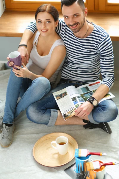 Attractive couple sitting on home floor looking at jurnal and smiling at each other.