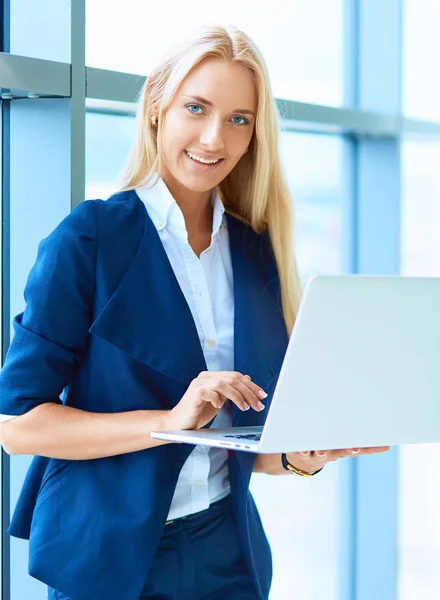 Femme d'affaires debout contre la fenêtre de bureau tenant ordinateur portable — Photo