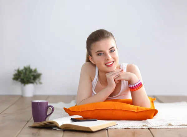 Lachende jonge vrouw liggend op een witte vloer met kussen — Stockfoto