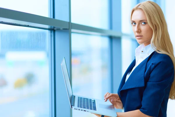 Femme d'affaires debout contre la fenêtre de bureau tenant ordinateur portable — Photo