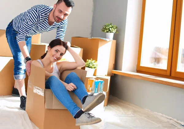 Casal feliz se divertindo e montando em caixas de papelão em nova casa — Fotografia de Stock