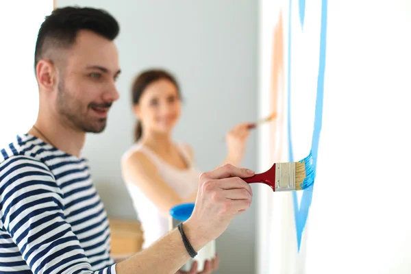 Porträtt av glada leende unga par målning innervägg av nya hus — Stockfoto