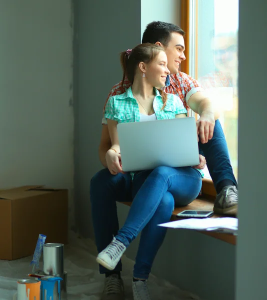 Portret van een jong koppel bewegen in nieuwe thuis zitten met laptop — Stockfoto