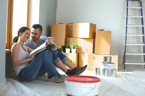 Atractiva pareja sentada en el piso de su casa mirando al juramento y sonriéndose mutuamente . —  Fotos de Stock