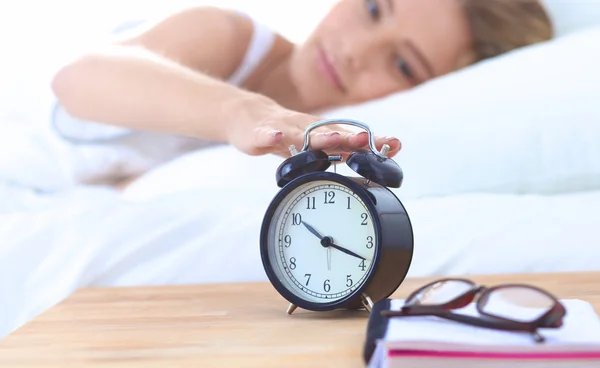 Jeune femme endormie et réveil dans la chambre à coucher à la maison Images De Stock Libres De Droits