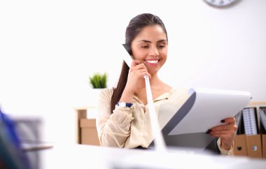 Genç iş kadını masada oturuyor ve telefonla konuşuyor.