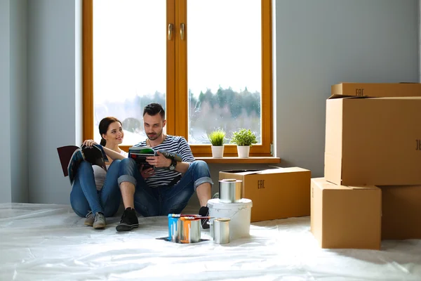 Ελκυστικό ζευγάρι που κάθεται στο πάτωμα το σπίτι βλέπουν jurnal και χαμογελώντας σε κάθε άλλο. — Φωτογραφία Αρχείου