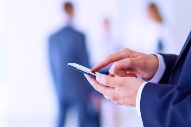 Ofisteki genç iş adamının portresi. Arka planda meslektaşları var ve cep telefonu kullanıyor.