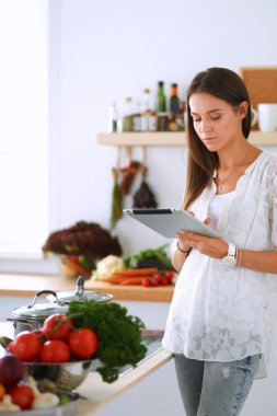 Mutfakta yemek yapmak için tablet bilgisayar kullanan genç bir kadın.