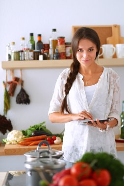 Mutfakta yemek yapmak için tablet bilgisayar kullanan genç bir kadın.