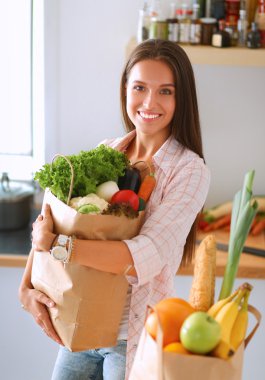 Elinde sebzeli alışveriş torbası tutan genç bir kadın.