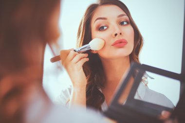 Genç ve güzel bir kadın aynanın yanında makyaj yapıyor.