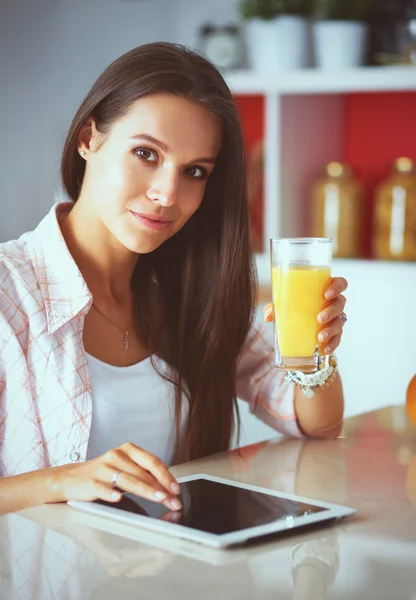 Femme utilisant un ordinateur tablette tout en buvant du thé dans sa cuisine — Photo